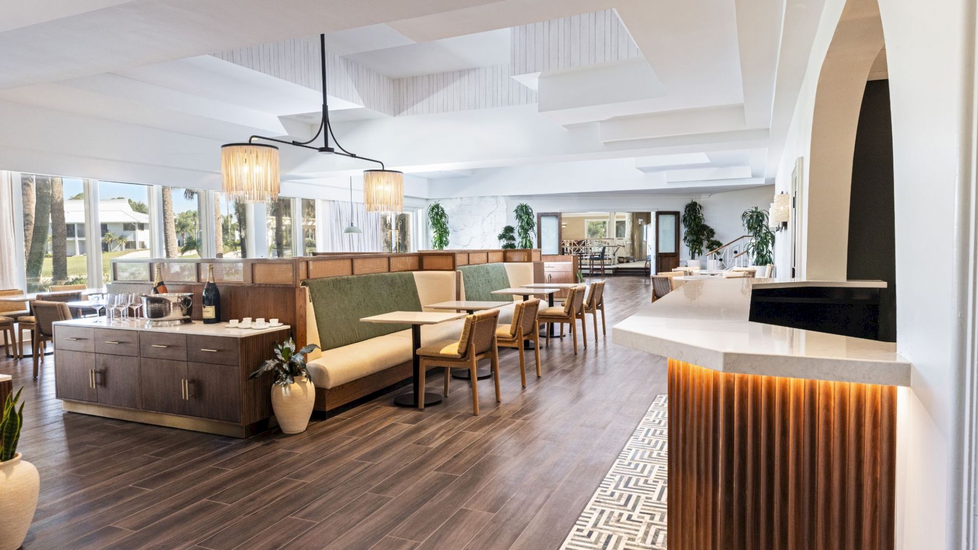 The image shows a modern, spacious interior with wooden floors, tables, chairs, and large windows, creating a welcoming atmosphere.